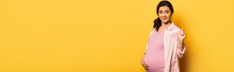 website header of pregnant woman touching belly and showing pregnancy test on yellow, horizontal image