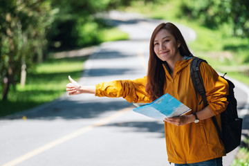 A young female traveler hitchhiking and stopping car with thumbs up on a mountains road