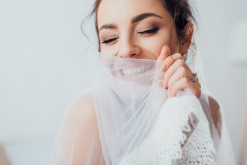 Selective focus of brunette bride with closed eyes holding lace veil