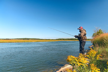 A fisherman on the shore of a reservoir is fishing on a sunny day. © Ann Stryzhekin