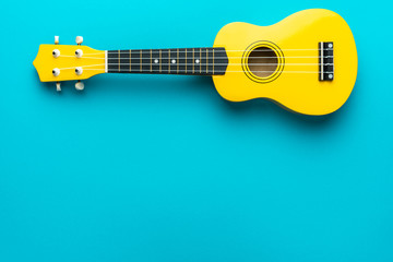 Yellow colored wooden ukulele guitar on the turquoise blue background. Overhead photo of ukulele with copy space. - obrazy, fototapety, plakaty