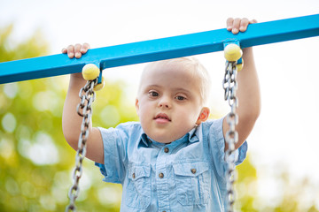 The daily life of a child with disabilities. A boy with Down syndrome plays in the playground....