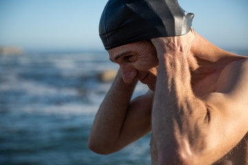 portrait of a man on the beach stretching out his swim cap.