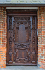 Old ornate wooden door with beautiful carvings. Dark wood entrance to the classic, vintage brick tenement house near torn market place in Polish Thorn (Torun).
