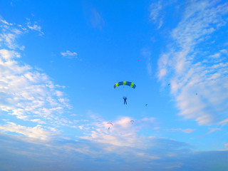 Naklejka na ściany i meble A skydiver with a bright multicolored parachute flies against the background of a blue sky with white sparse clouds