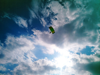 A skydiver with a bright multicolored parachute flies against the background of a blue sky with white sparse clouds