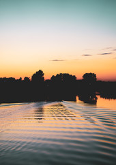 Silhouette of a motor, rubber boat at sunset over the lake. Smooth water surface torn by the waves....