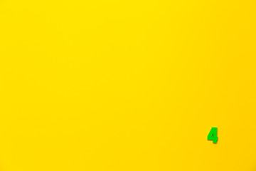 Number 4, four, the fourth of the plastic baby green toy number is located in the lower right corner on a yellow paper background. Banner on the topic of page numbering, timing or day in the calendar