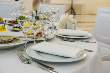 beautiful table setting in light colors with dishes and assorted food on a table with a white tablecloth for a party, wedding or other special event. Restaurant business and service industry concept.