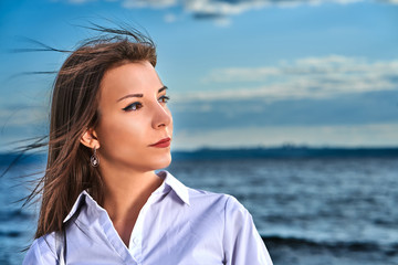 Portrait of a young brunette girl against the background of the evening sky over the sea. Close-up of the girl's face.