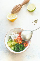 Bowl with spoon and fresh ingredients: avocado, coriander, tomato, onion. Lemon, lime, pepper and wooden citrus press in background. Healthy food concept in summer.  White background. Top view
