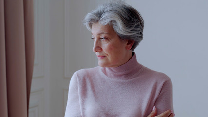 Beautiful old woman with gray hair smiles standing at home