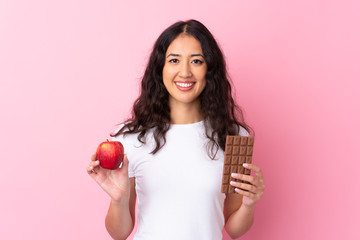 Spanish Chinese woman over isolated pink background taking a chocolate tablet in one hand and an...