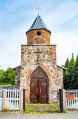 Fototapeta premium Small vintage christian catholic chapel. Brick building with gothic wooden gate with fittings.Worship village building. Old religion prayer church.