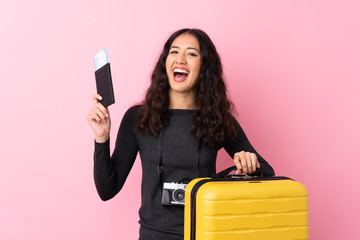 Mixed race woman over isolated pink background in vacation with suitcase and passport