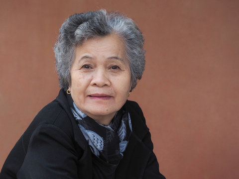 Asian senior woman smiling and looking at camera while sitting on chair