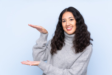 Spanish Chinese woman over isolated blue background holding copyspace to insert an ad