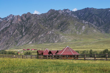 Fototapeta na wymiar Small hexagonal log cabins for tourists stand against the backdrop of the mountain slopes. Travel the Altai Republic of Russia during the summer months.