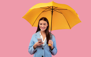 Portrait of smiling young girl holding umbrella using phone