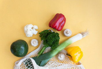 Set of vegetables cauliflower, sweet pepper, tomatoes, leeks, avocado, mushrooms, parsley for healthy food in a bag of string bags on a yellow background. Concept of healthy food purchases. 
