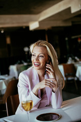 Beautiful businesswoman dressed in the suit drinking wine and talking to the phone. Businessman and businesswoman enjoying in the restaurant.