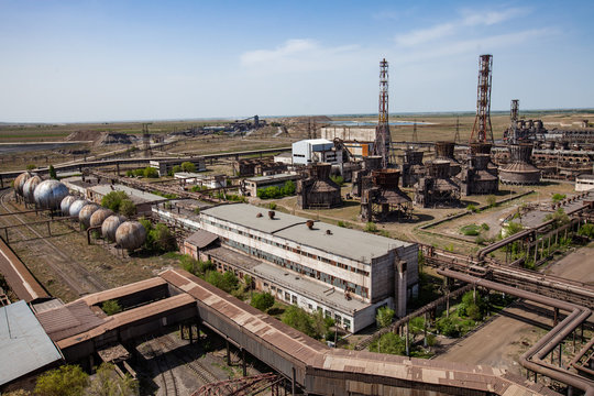 Old soviet outdated metallurgy industrial buildings and rusted cooling towers, factory chimneys and pipelines. Blue sky. Taraz city, Kazakhstan.