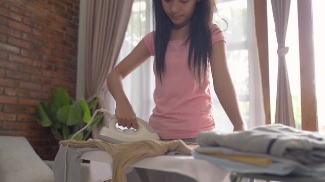 Smiling teen girl ironing clothes to do household on the ironing board in the room at home