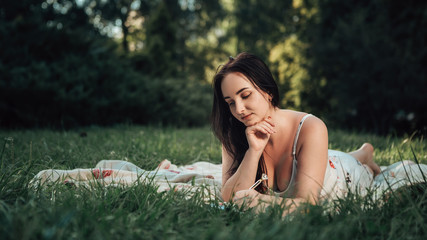 Close up portrait of young woman lying on the soft cevrlet and taking notes. Dreamy lady in the city park writing something. Image with copy space and blur background.