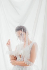 Bride in wedding dress and veil looking at camera near white cloth