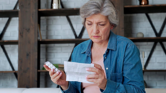 An elderly woman with tablets in her hands and reads a prescription medication.