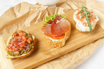 
Nice food. Bruschetta with ham, salmon and pesto on a wooden board. Close-up.