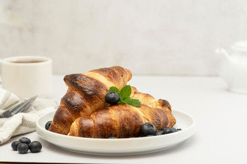 Breakfast with fresh croissants, tea and blueberry on bright background. Pastry, buns.