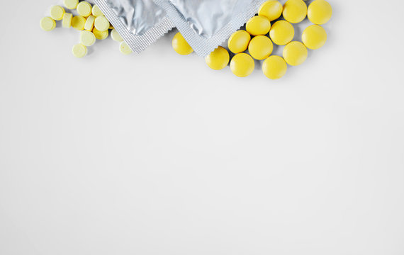 Two Condoms And A Bunch Of Round Large And Small Yellow Pills On  White Background With Copy Space. Use And Condom Of Pills To Reduce The Likelihood Of Pregnancy Or For Sexually Transmitted Diseases.