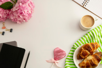 Table top of work space frame with cup of coffee, croissants, pink hydrangea and notebooks.