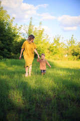 Cute baby boy and mother walking on green lawn. Summertime photography for ad or blog about motherhood