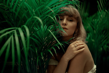 Woman in palm leaves. Model's face in green. Fashion photo of a girl in the tropics