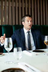 Handsome businessman dressed in the suit drinking wine. Businessman and businesswoman enjoying in the restaurant.