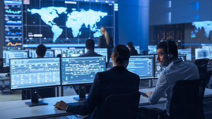 Team of Professional Computer Data Science Engineers Work on Desktops with Screens Showing Charts, Graphs, Infographics, Technical Business Data and Statistics. Low Key Control and Monitoring Room.