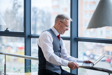 Adult male businessman, teacher, mentor working on a new project. Sits by a large window on the...