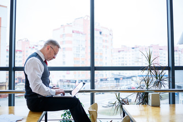 Adult male businessman, teacher, mentor working on a new project. Sits by a large window on the...