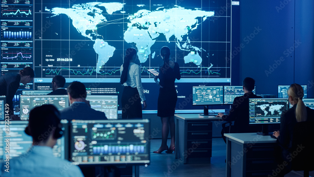 Poster Project Manager and Computer Science Engineer Talking while Using Big Screen Display Showing Global Map and Data. Telecommunications Company System Control and Monitoring Room.