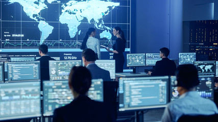 Project Manager and Computer Science Engineer Talking while Using Big Screen Display Showing Global Map and Data. Telecommunications Company System Control and Monitoring Room.