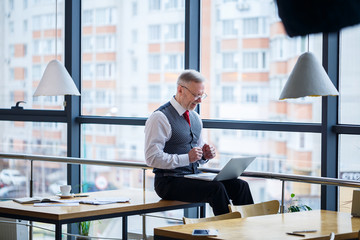Adult male businessman, teacher, mentor working on a new project. Sits by a large window on the...