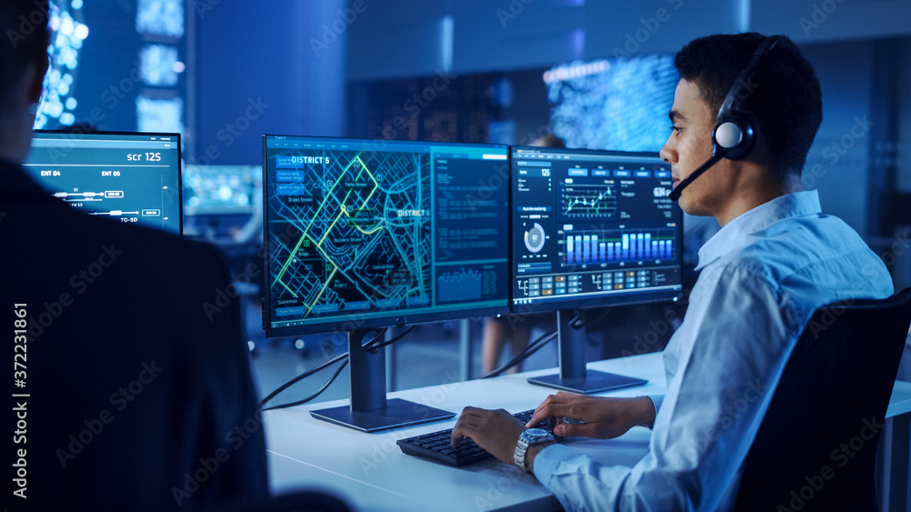 Poster confident male data scientist works on personal computer wearing a headset in big infrastructure con