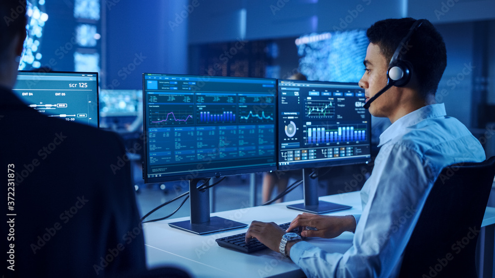 Poster confident male data scientist works on personal computer wearing a headset in big infrastructure con