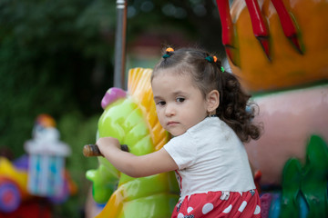 Adorable little toddler girl riding on animal on roundabout carousel in amusement park. Happy healthy baby child having fun outdoors on sunny day. Family weekend or vacations