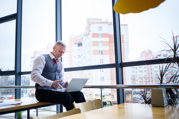 Adult male businessman, teacher, mentor working on a new project. Sits by a large window on the...