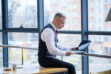 Adult male businessman, teacher, mentor working on a new project. Sits by a large window on the...