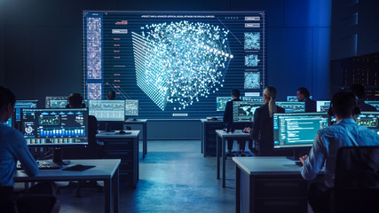 Team of Professional Computer Data Science Engineers Work on Desktops with Screens Showing Charts, Graphs, Infographics, Technical Neural Network Data and Statistics. Dark Control and Monitoring Room.