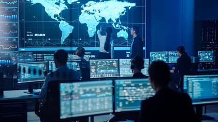 Project Manager and Computer Science Engineer Talking while Using Big Screen Display Showing Global Map and Data. Telecommunications Company System Control and Monitoring Room.